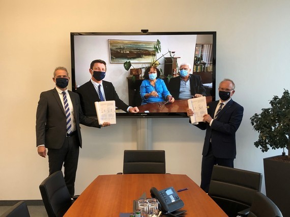 Vier Personen in einem Konferenzraum halten Dokumente und stehen vor einem Bildschirm mit einer Landschaftsaufnahme.