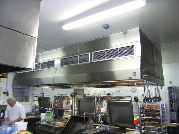 Eine professionelle Küche mit Edelstahlgeräten, Arbeitsplätzen und Kochen im Hintergrund.