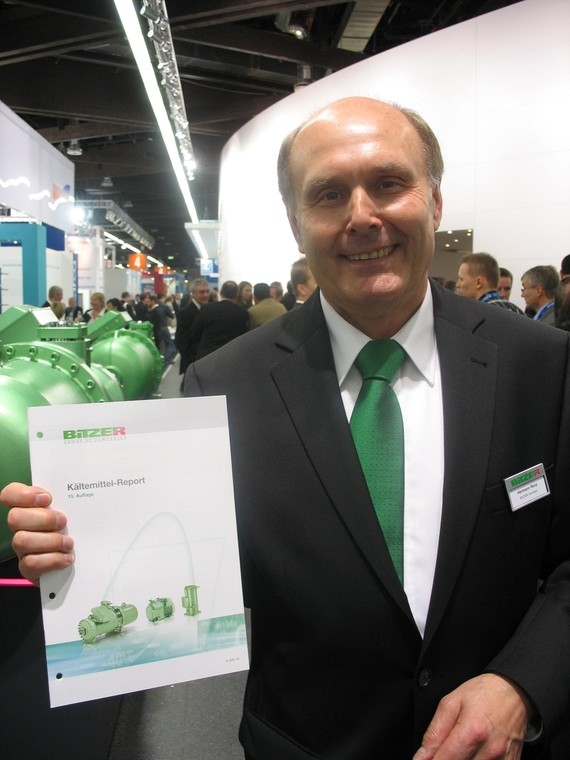 Ein Mann im Anzug hält ein Dokument mit grünen Symbolen und steht in einem belebten Veranstaltungsort.