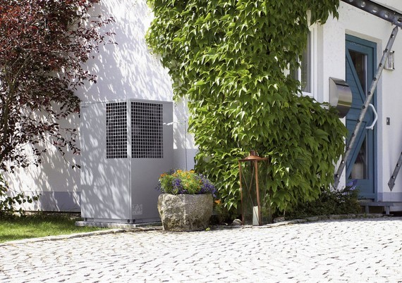 Ein weißes Gebäude mit einem großen Fenster, grüner Vegetation und einem Klimagerät an der Wand.