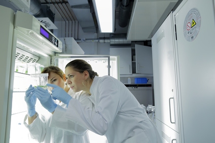 Zwei Personen in Laborkleidung arbeiten in einem Labor, wobei eine Person eine Probe in einer Pipette hält.