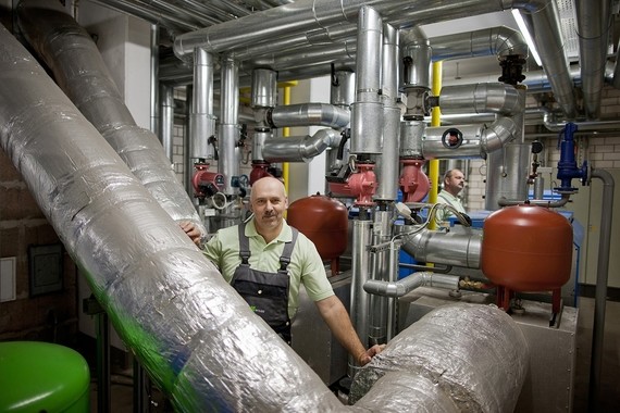 Ein Mann steht in einer technischen Anlage mit vielen Rohren und Geräten.