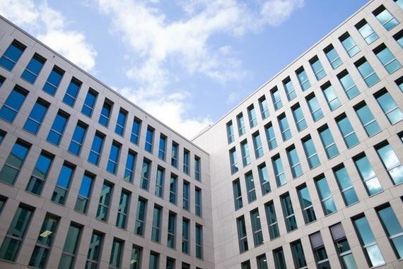 Zwei moderne Bürogebäude mit großen Fensterfronten stehen unter einem blauen Himmel mit einigen Wolken.