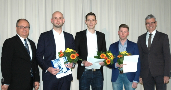 Fünf Personen in Anzügen stehen nebeneinander, wobei drei von ihnen Urkunden halten und Blumensträuße präsentieren.
