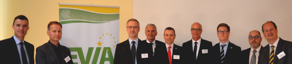 Ein Gruppenbild von sieben Männern in Anzügen vor einem grünen Hintergrund mit dem Logo 