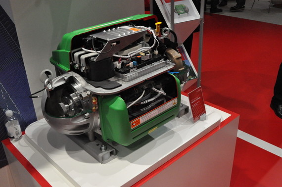 Ein grüner Motorblock mit sichtbaren Komponenten steht auf einem Podest.