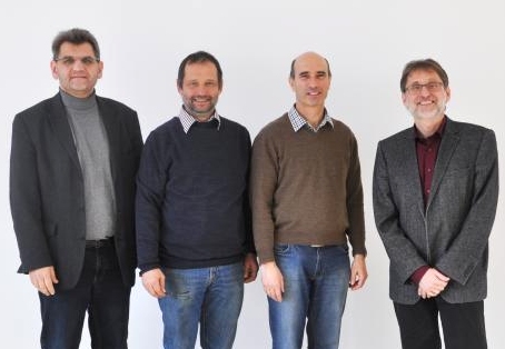 Vier Männer stehen nebeneinander vor einem neutralen Hintergrund.