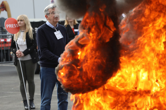 Zwei Personen stehen im Hintergrund, während im Vordergrund ein Feuer brennt.