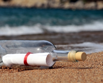 Eine Flaschenpost mit einem Zettel liegt am Strand vor dem Meer.