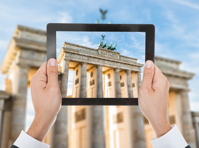 Zwei Hände halten ein Tablet, auf dem das Brandenburger Tor zu sehen ist.