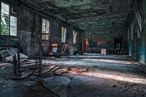 Ein verlassenes, verfallenes Gebäude mit zerstörten Wänden, alten Möbeln und Tageslicht, das durch Fenster einfällt.