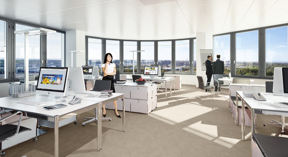 Ein helles, modernes Büro mit großen Fenstern, Arbeitsplätzen und Mitarbeitern, die sich unterhalten.