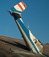 Ein umgekipptes Flugzeug mit blau-weißem Rumpf und rotem und weißen Streifen auf dem Rumpf liegt auf einem Dach.