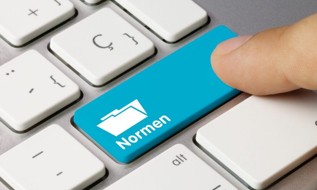 Ein Finger drückt eine Tastatur-Taste mit dem Symbol und dem Text "Normen".
