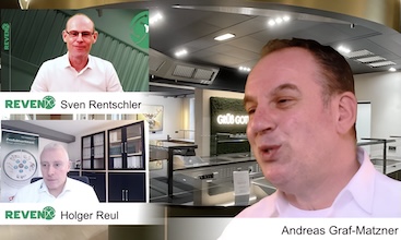 Zwei Personen führen ein Interview in einem modernen Büro, wobei der Hintergrund mit technischen Geräten und einem Fenster sichtbar ist.