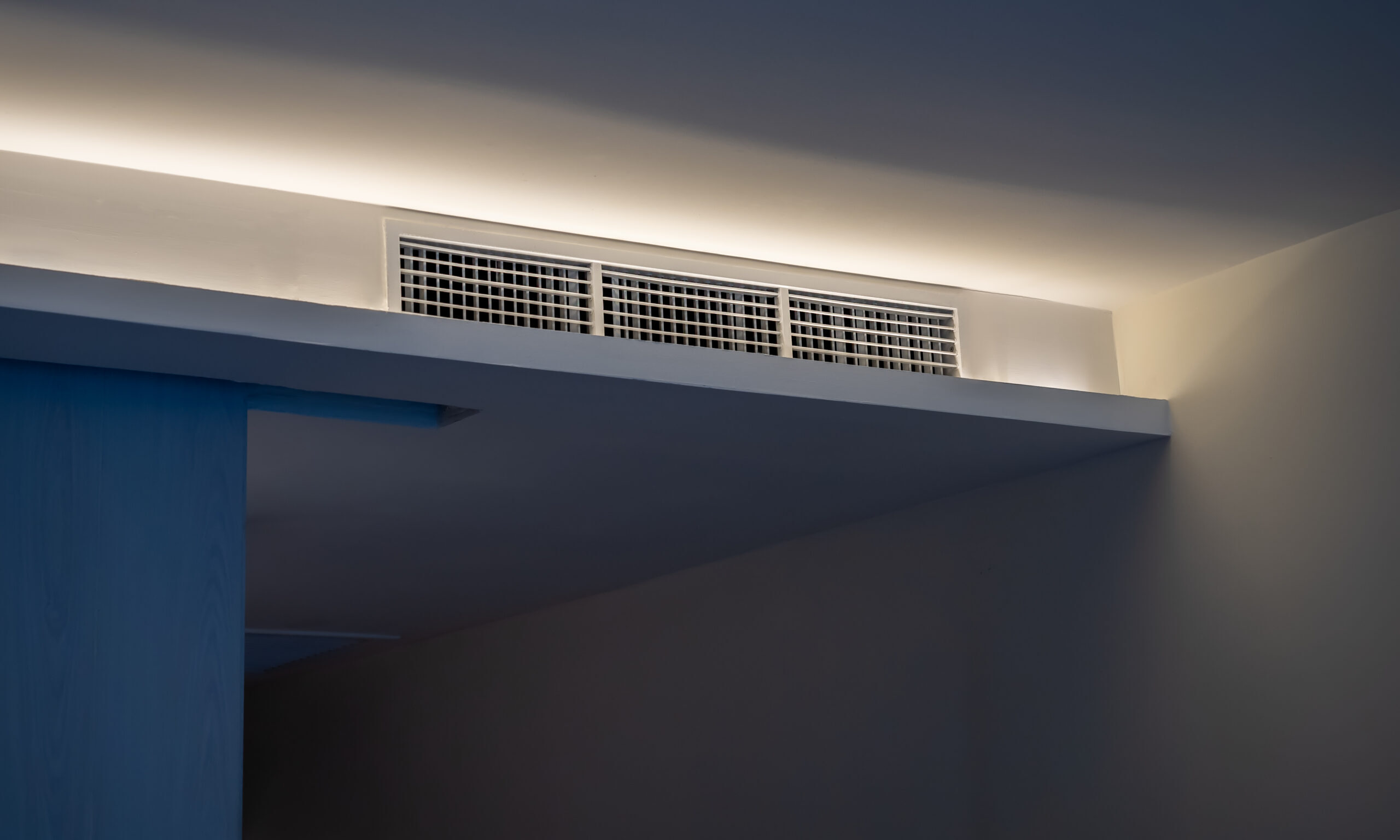 Air conditioning wall mounted ventilation system on ceiling in the white hotel room with dim light. Hotel room air ventilation grill on the wall.