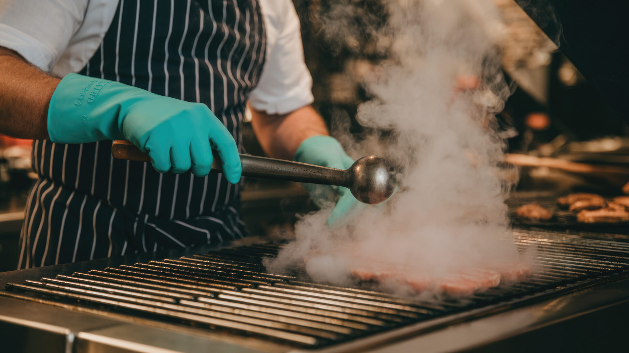 Man grilling meat on a commercial grill with smoke